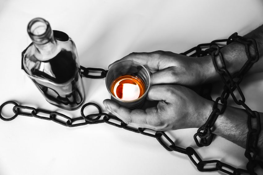 Man's hands in old rusty chains near the bottle. Addicted to alcohol. Dangerous habit.